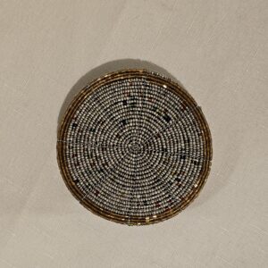 Handmade white, black, and multi-color beaded coaster intricately woven and polished for decorative or functional use.